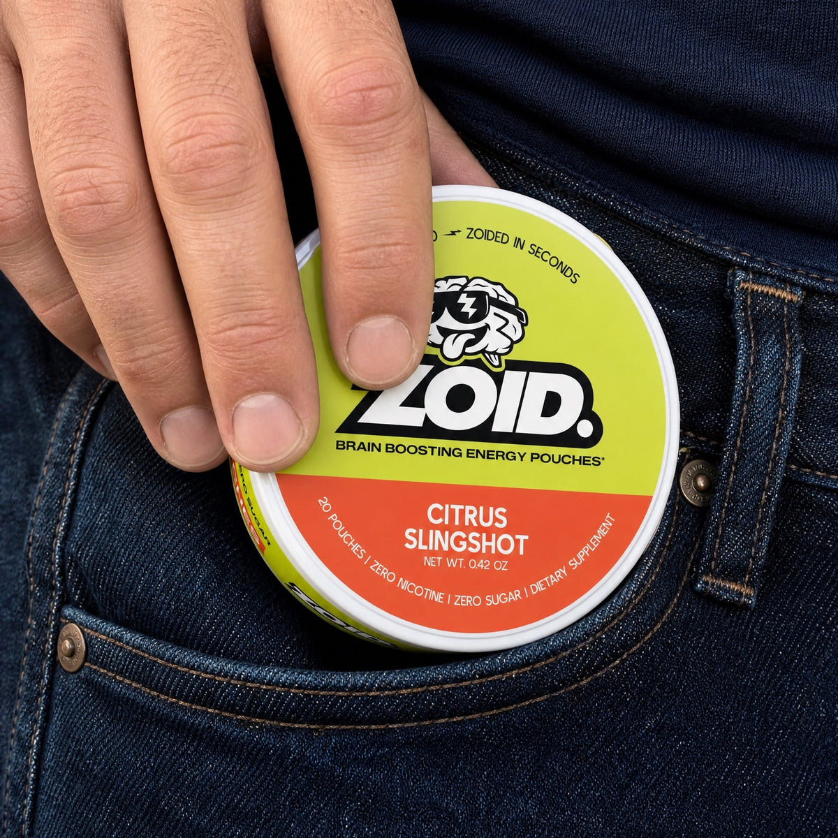 A close-up of a hand placing a round tin of Zoid Citrus Slingshot brain boosting energy pouches into the pocket of dark blue jeans.